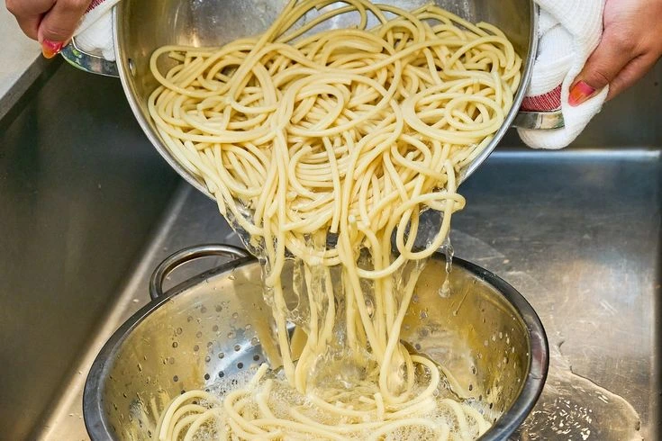 un uomo sciacquò gli spaghetti in una ciotola